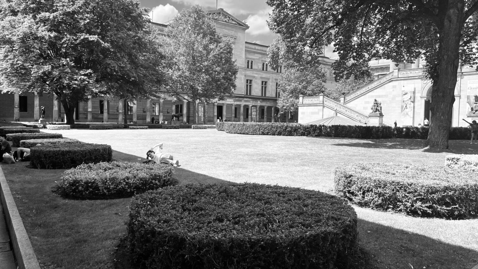 Black and white photo of the gardens outside the Neues Museum in Berlin, with lawns, hedges and the museum building in the background