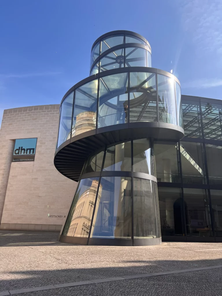 Glass spiral staircase tower on the facade of a modern stone building, seen from the street